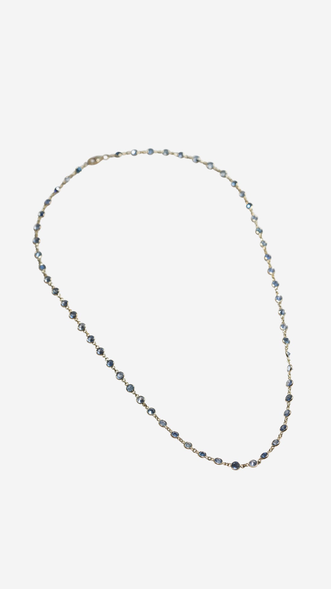 ILA SODHANI Capri necklace shown clasped and laid flat on a white background; natural blue sapphires set with yellow gold chain.