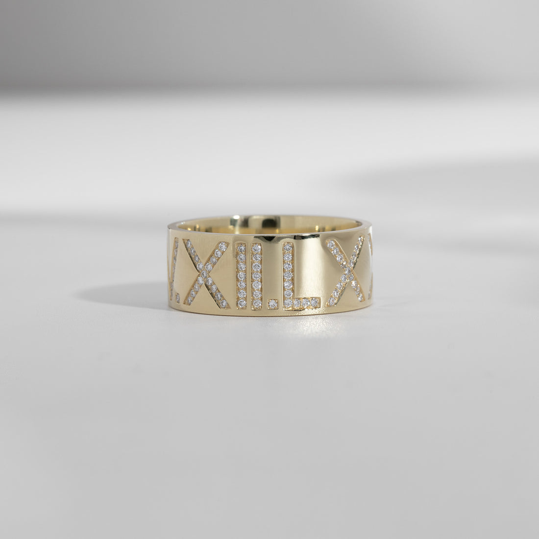 An ILA SODHANI Celebration Diamond Ring in yellow gold with white diamonds set into the roman numerals, "V.XII.LX"; shown in front of a white background.