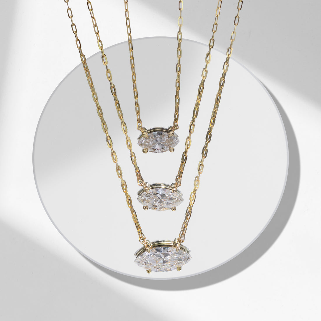 Three ILA SODHANI Protection Necklaces with different sized eye-shaped natural diamonds hanging from yellow gold chains; the necklaces are hanging stacked over a white plate.