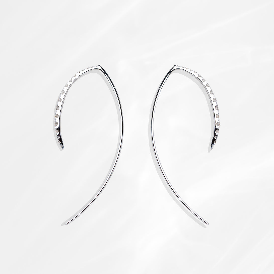 Two ILA SODHANI Khale Earrings shown laid on their sides with the diamonds facing away from each other; visible from this angle is the white gold of the threader post and the edges of the diamonds set onto the fronts.
