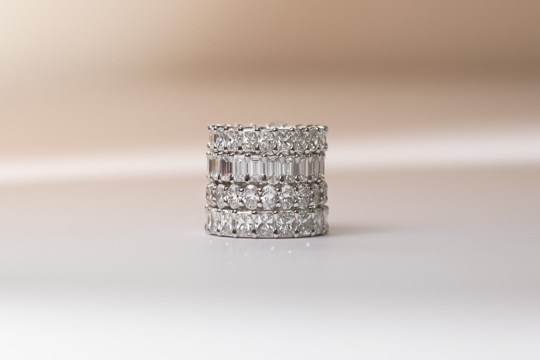 Four ILA SODHANI Latitude 0 bands stacked atop each other in white gold with natural diamonds; from top to bottom: radiant cut, emerald cut, oval cut, and a wider radiant cut than the top ring.