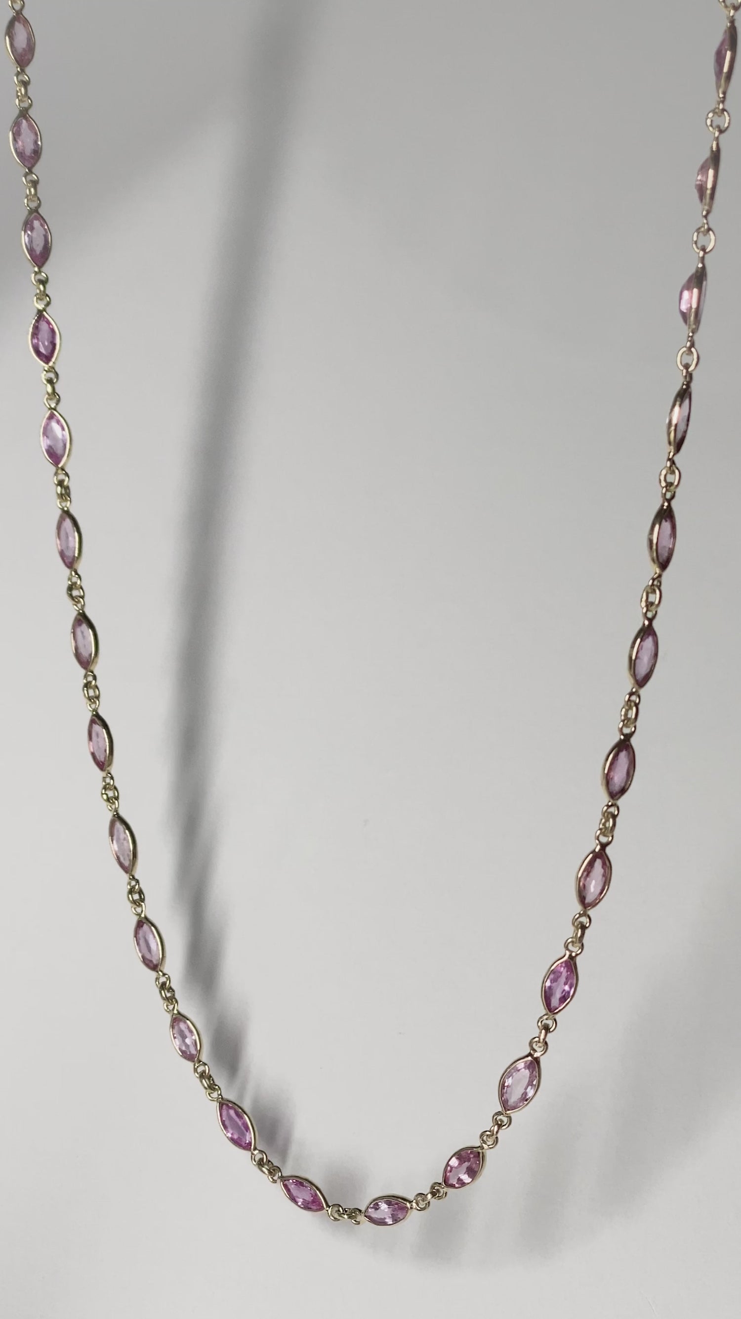ILA SODHANI Camilla necklace with marquise cut natural pink sapphires set in yellow gold is shown hanging in front of a white background, swaying gently in the light.