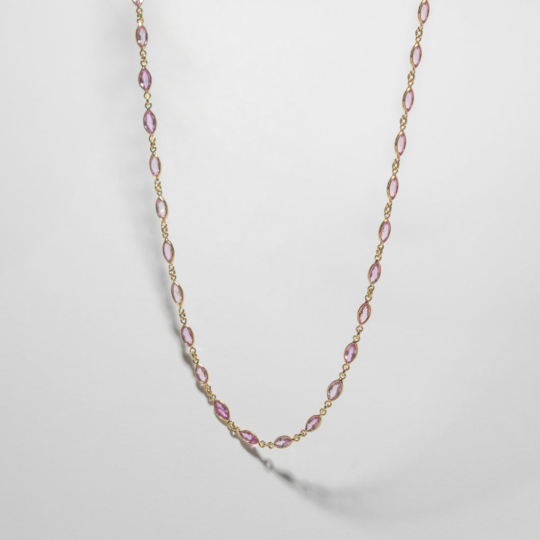 ILA SODHANI Camellia Necklace with marquise cut natural pink sapphires set in yellow gold; shown hanging in front of a white background.